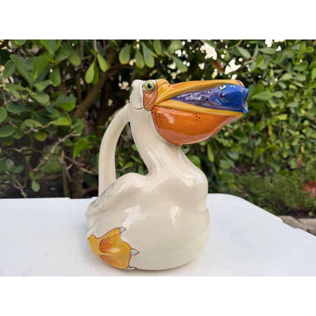 Decorative ceramic pelican pitcher by Animals & Co., featuring a colorful hand-painted coastal design with a fish-form...