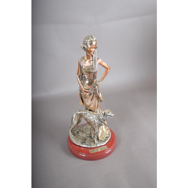 Art Deco revival sculpture depicting a poised woman in a draped gown beside a Borzoi dog. Both figures are silver-plated...