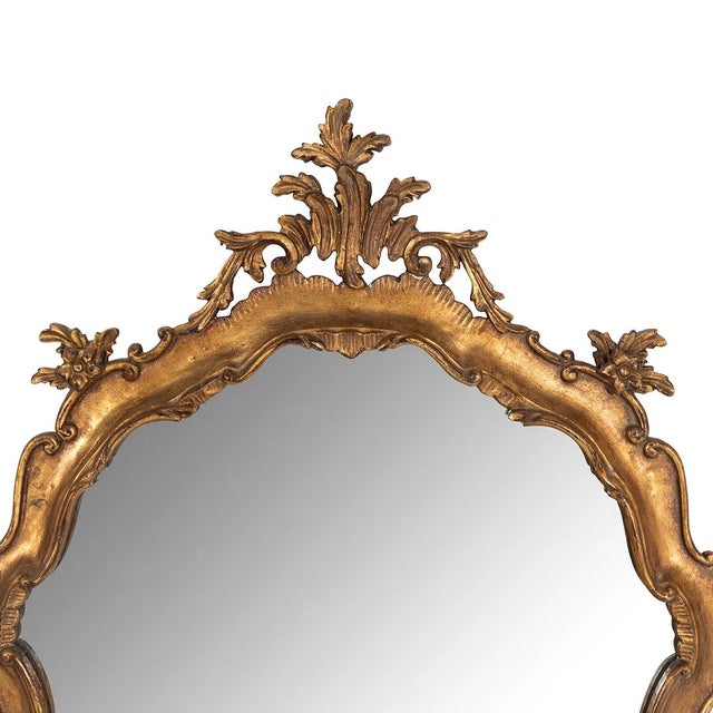 A beautifully carved Venetian style giltwood wall mirror featuring an elegant Rococo-inspired silhouette with flowing...