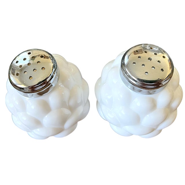 A sculptural pair of vintage milk glass salt and pepper shakers with rounded bodies covered in overlapping, leaf-like...