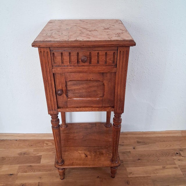 Charming french bedside table from around 1900 with a decorative marble top and elegant fluted legs. Designed in the...