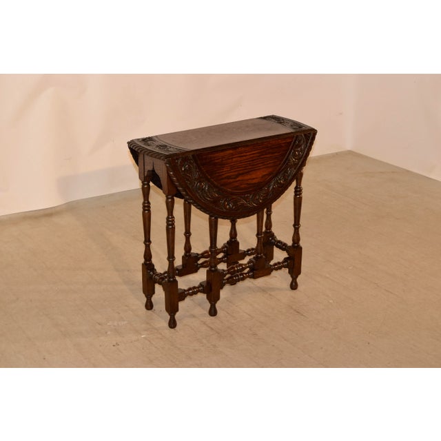 19th century oak gate leg from England with a carved and beveled edge surrounding the carved banded top. The apron is...