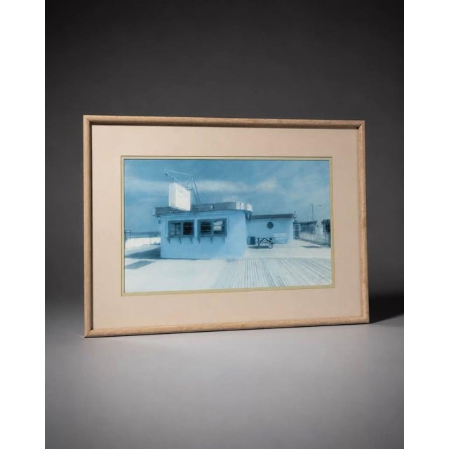 Large framed coastal boardwalk print featuring a soft blue beachside building scene with an airy, calm, and relaxed...