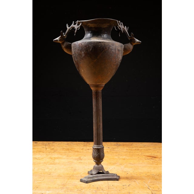 Antique cast metal jardinière featuring a deep urn-shaped basin, two stag-head handles, and antlers extending to the rim....