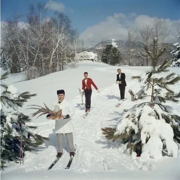 Skiing Waiters 1960 Three skiing waiters on a ski slope, with the man in the foreground carrying a bird on a tray, the...