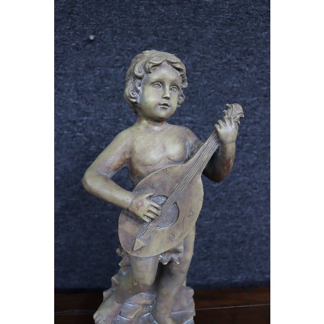 Italian figure depicting a standing putti playing a mandolin while standing atop a rocky naturalistic base. Finished in...