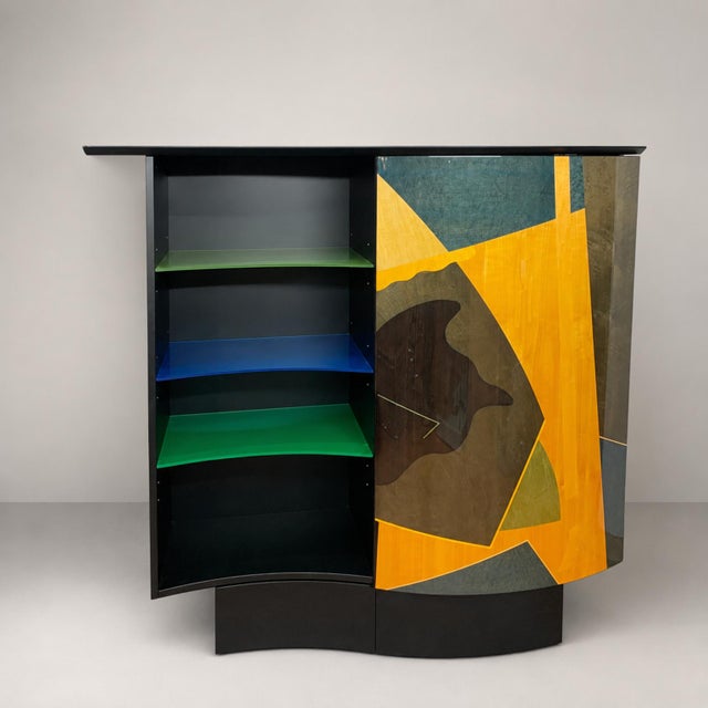 A curved structure in black lacquered wood with a large curved door inlaid with various colored woods. The left...