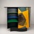 A curved structure in black lacquered wood with a large curved door inlaid with various colored woods. The left...
