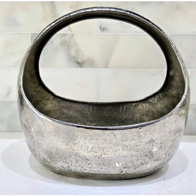 Striking vintage-style sculptural basket bowl in hammered silver metal, featuring a bold oval form and integrated handle...