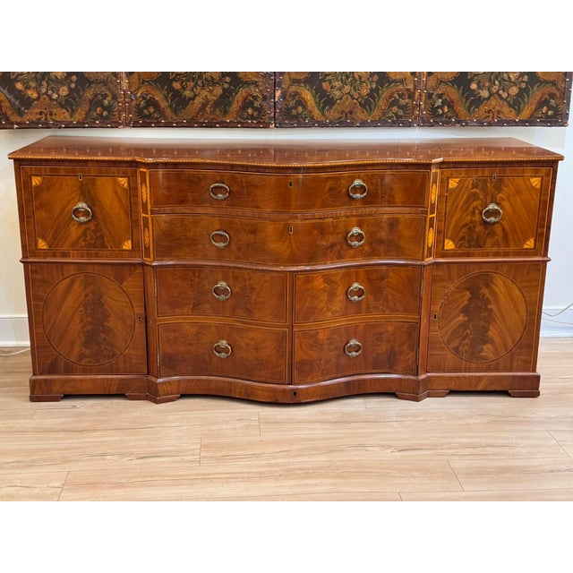 An unusual late 18th century English mahogany sideboard/commode with a serpentine front and satinwood inlay, the top edged...