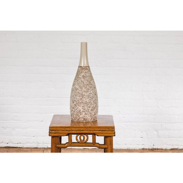 An artisan made bottle-shaped ceramic vase with light brown background and energetic cream dripping. This contemporary,...