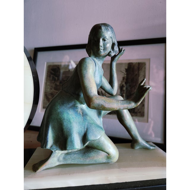 Art Deco figural marble mantel clock featuring a patinated bronze or spelter sculpture of a seated young girl, created by...