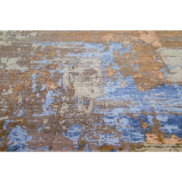 This Indian wool and silk blend rug features a brown field with an abstract pattern detailing orange and blue colors. Its...