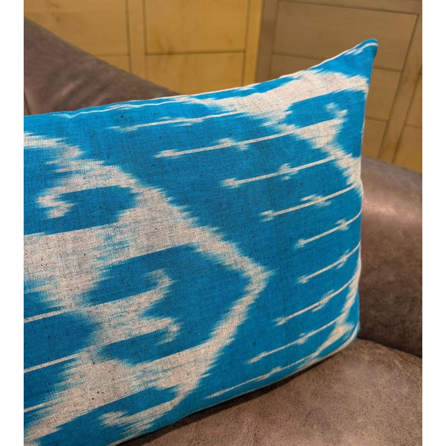 Angular chevron shapes and sharp zigzag lines expand outward from a wide open white center field, all woven in sky blue...