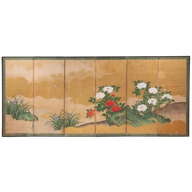 A six panel Japanese screen depicting a landscape scene peonies and sparrows against a gold backdrop of clouds and sky....