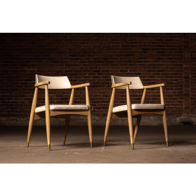 Sculptural mid century modern dining armchairs executed in walnut with tapered round legs, integrated curved armrests, and...