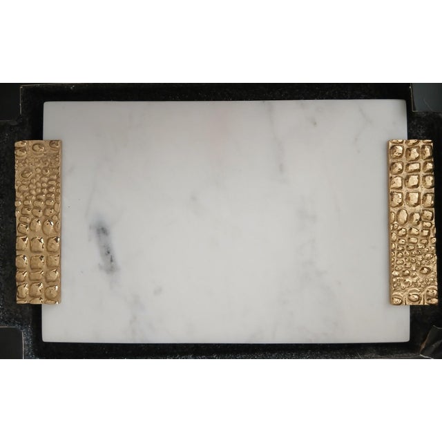 Michael Aram cheese board featuring a white marble surface with textured gold-tone handles from the Safari Collection. The...