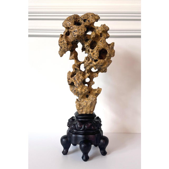 A Chinese Taihu scholar rock is displayed on a carved wood base in an vertical form. Well-balanced and resembling a...