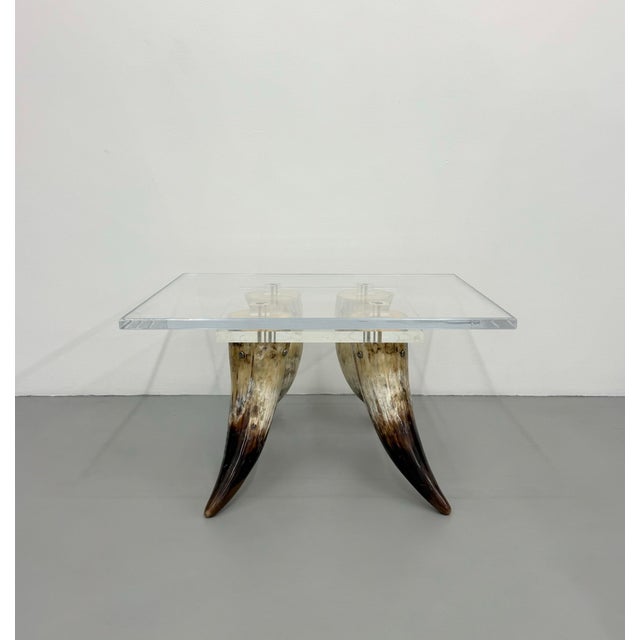 A striking vintage side table featuring a thick square Lucite top supported by four sculptural natural horn legs with rich...
