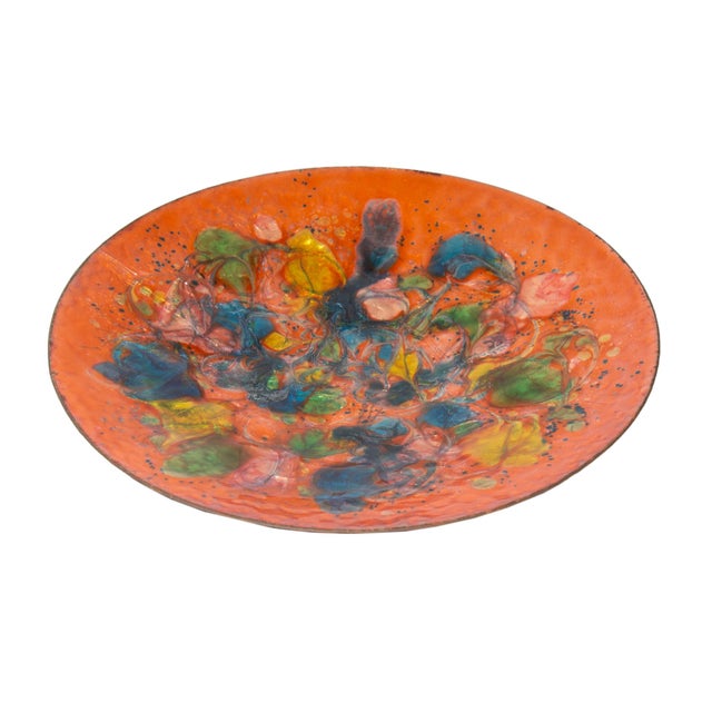 A Mid-Century orange enamel plate with vibrant splashes of color. The underside and rim of the plate are black. The entire...
