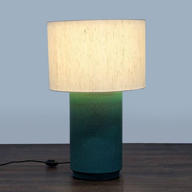 This CB2 table lamp features a simple white drum shade and a stylish green gradient ceramic base. It offers a clean,...