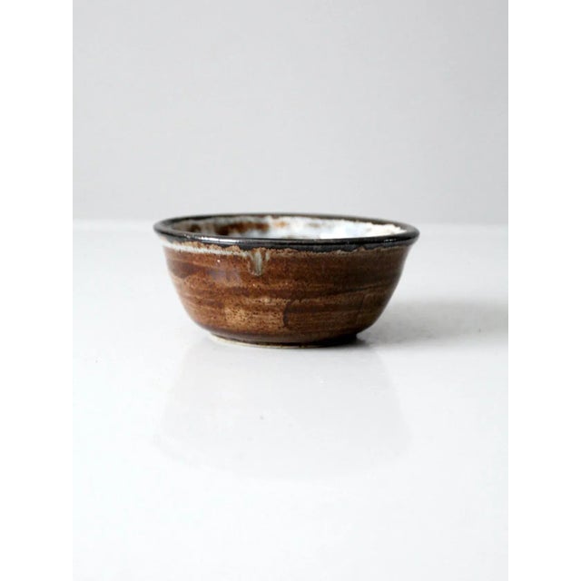 This hand-crafted studio pottery bowl features a warm brown-washed exterior glaze, accented by a bold black rim. The...