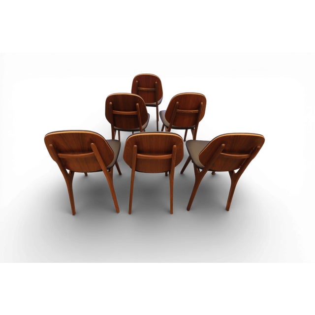 The chair is model No. 75 and is made of teak with dark tones on the frame and rounded cushions. A set of four chairs in a...