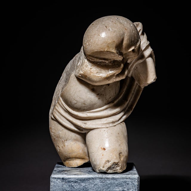 Small marble sculpture preserved in fragmentary condition and mounted on a modern stone cube base. The surviving torso...