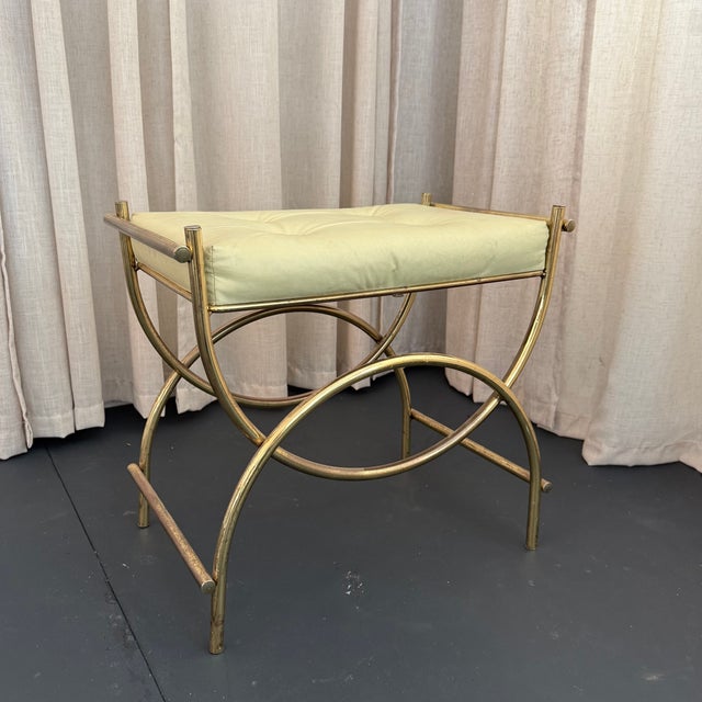 This decorative Hollywood Regency vanity stool features a sweeping, brass toned frame that follows the format of an...