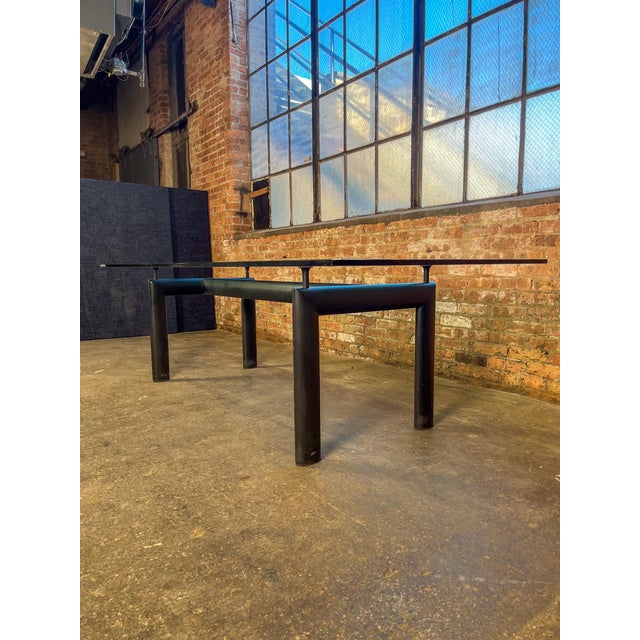 Dining table attributed to Le Corbusier, featuring a thick rectangular glass top resting on a sculptural black steel base....
