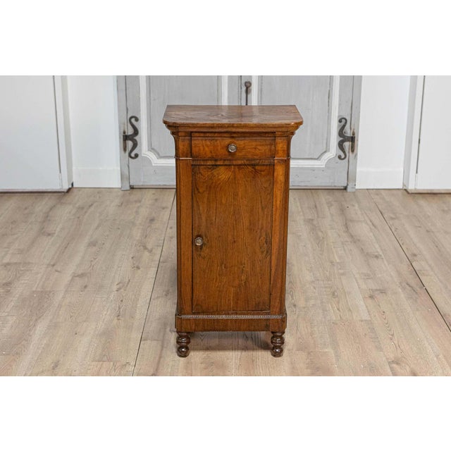 An Italian walnut bedside table from the 19th century with single drawer over single door and carved reeded motifs. This...
