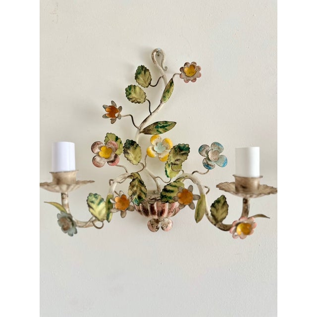Pair of vintage floral tole wall sconces in painted metal, with colorful flowers and green foliage arranged above ribbed...