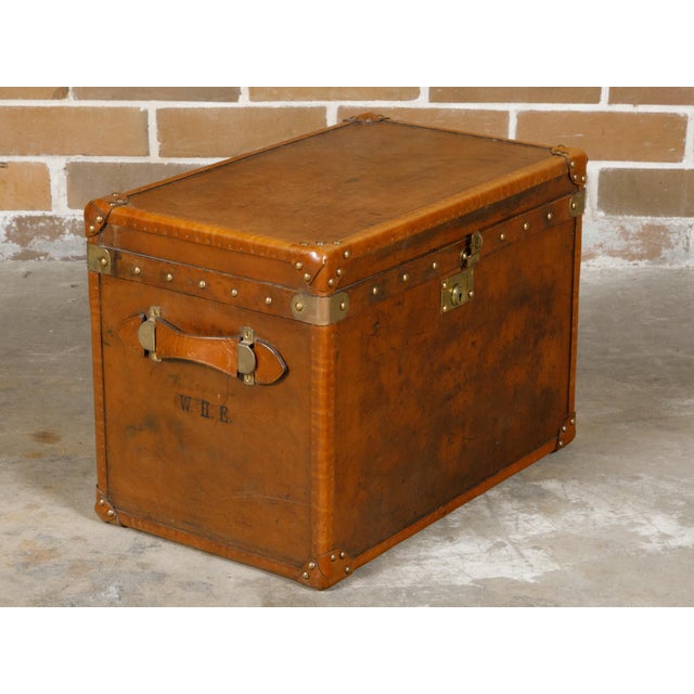 An English Turn of the Century leather trunk from circa 1900 with brass accents, lateral handles and monogram. This...