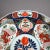 An antique Asian Imari charger offers porcelain construction with hand painted garden reserves, gilt highlights and en...