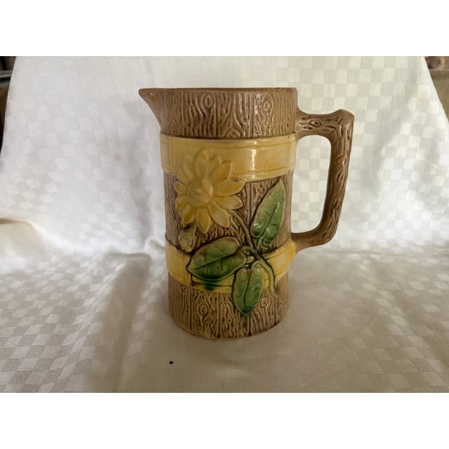 This is a classic majolica cream or milk pitcher. pitcher, . It has a simulated banded wood background on which a daisy...