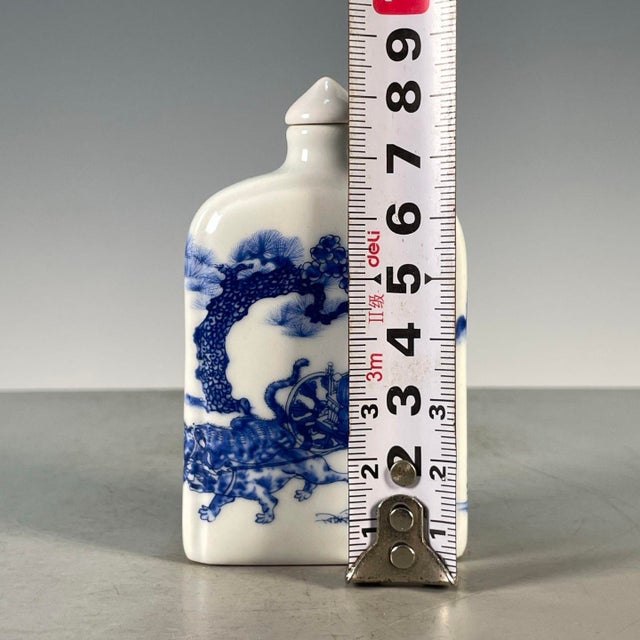 This is a charming vintage porcelain snuff bottle, decorated in the classic blue and white palette. The bottle features a...