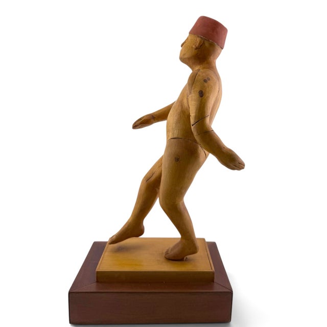 Donald Nelsen painted wood carving depicting a walking male figure wearing a traditional red fez, mounted on a two-tone...