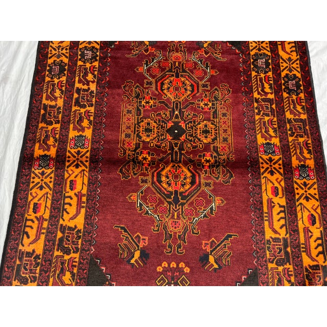 This eye-catching vintage Afghan Baluchi rug features a rich tribal pattern with deep burgundy and amber tones, accented...
