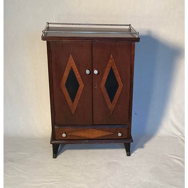Mid Century Modern walnut veneer cabinet, features Art Deco design elements, a top chrome railing and a lower drawer. Two...