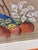 Features a pensive female figure rendered in soft earth tones with graceful drapery.Accented with earthen vessels and...