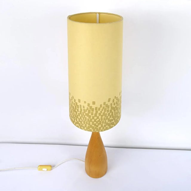 This elegantly shaped lamp foot has a slim waist and carries a soft yellow conic shade of which the bottom part is set...