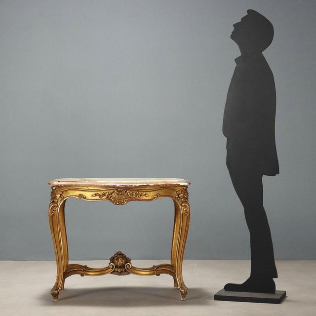 A late Baroque-style coffee table in carved and gilded wood. A recessed white marble top rests on four curved legs carved...