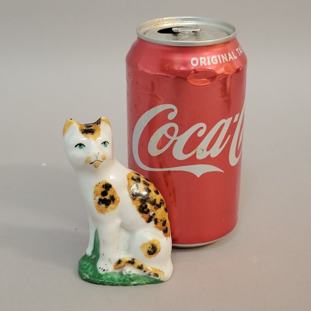 An antique English Staffordshire cat figure seated upright with an alert posture and gently expressive features. The...