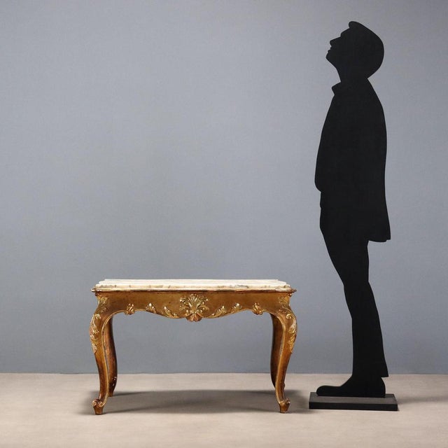 Late Baroque-style coffee table in carved and gilded fir wood. The marble top is inset and supported by four curved legs...