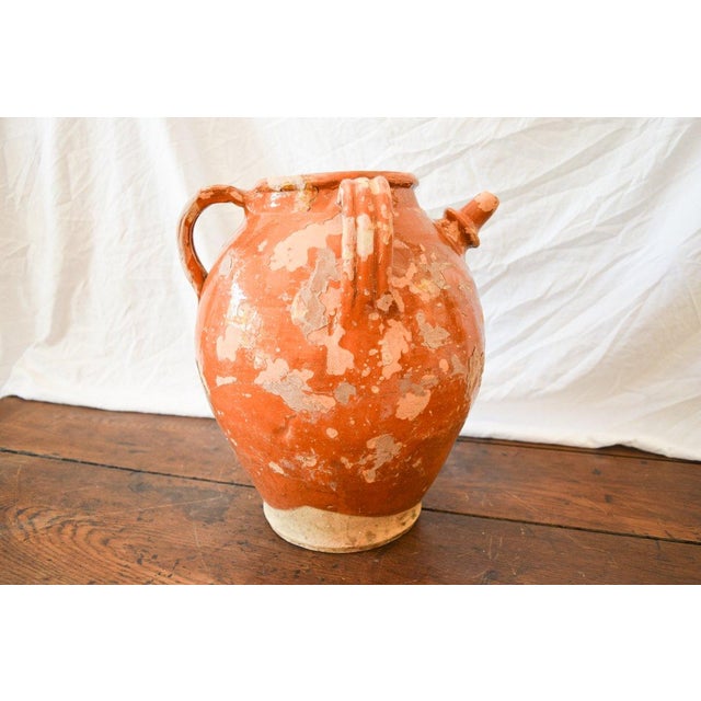 Rustic earthenware pottery with small spout and two handles. Rust colored glaze.