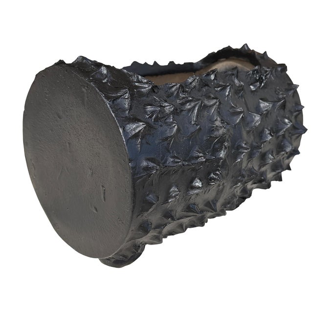A sculptural black faux bois concrete planter modeled as a hollowed horizontal log, with pronounced bark-like texture,...