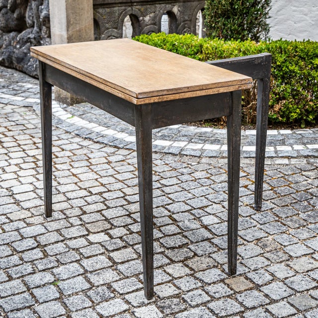 Painted folding table in dark gray and light brown, featuring four square tapered legs and a straight apron. One leg...