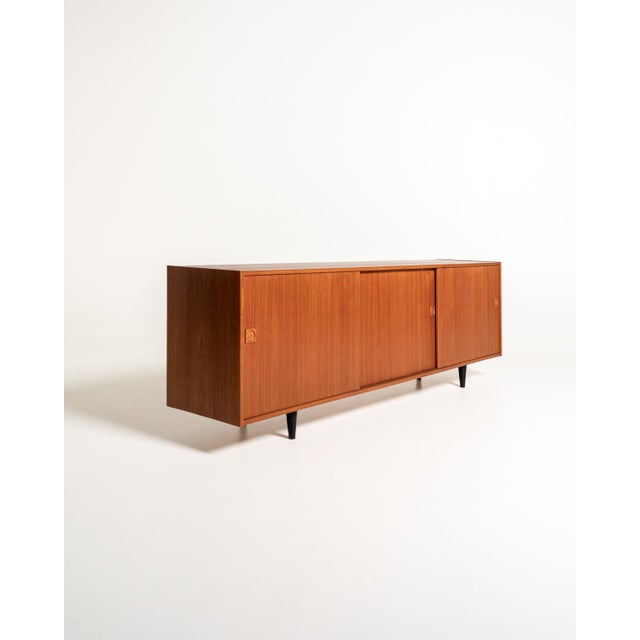 Teak sideboard with three sliding doors and recessed handles, supported by low, turned, black-lacquered legs. Danish...