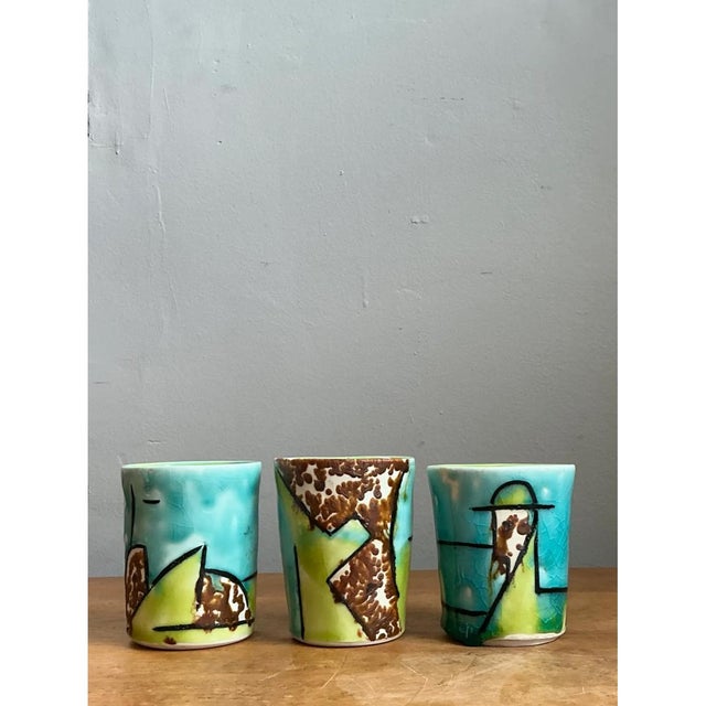 This set of cylindrical cups showcases bold, hand-painted abstraction in a vivid palette of turquoise and lime green, each...