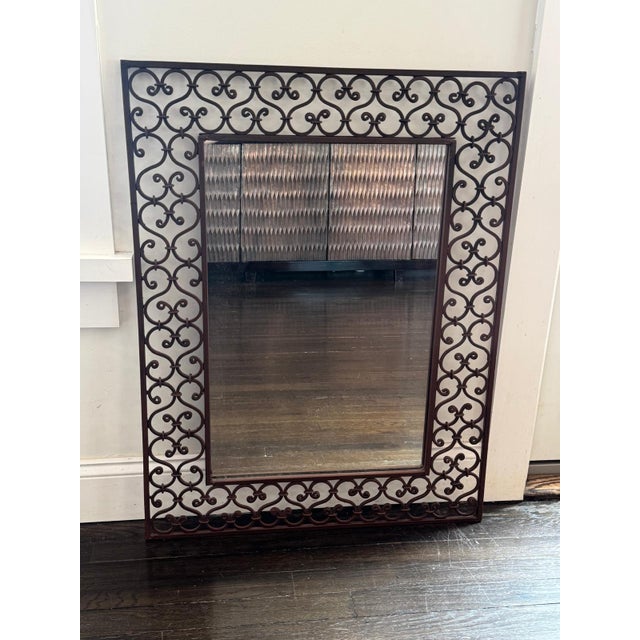 Decorative wrought iron wall mirror featuring an elegant scrolling motif and bronze finish. The intricate openwork frame...